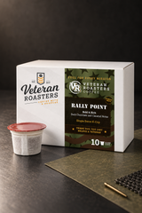 Angled view of the Rally Point darkest roast K-Cups 10-count box, with a coffee pod, map notebook and dog tags.